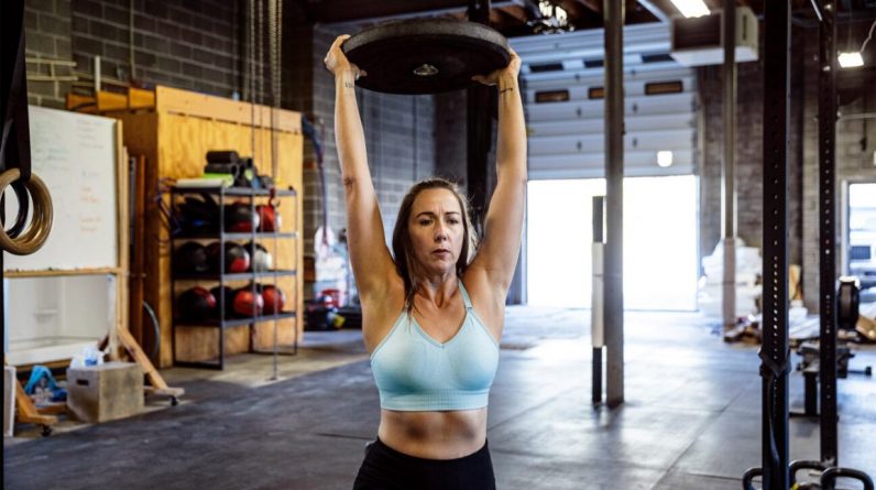 A younger woman lifts a weight over her head